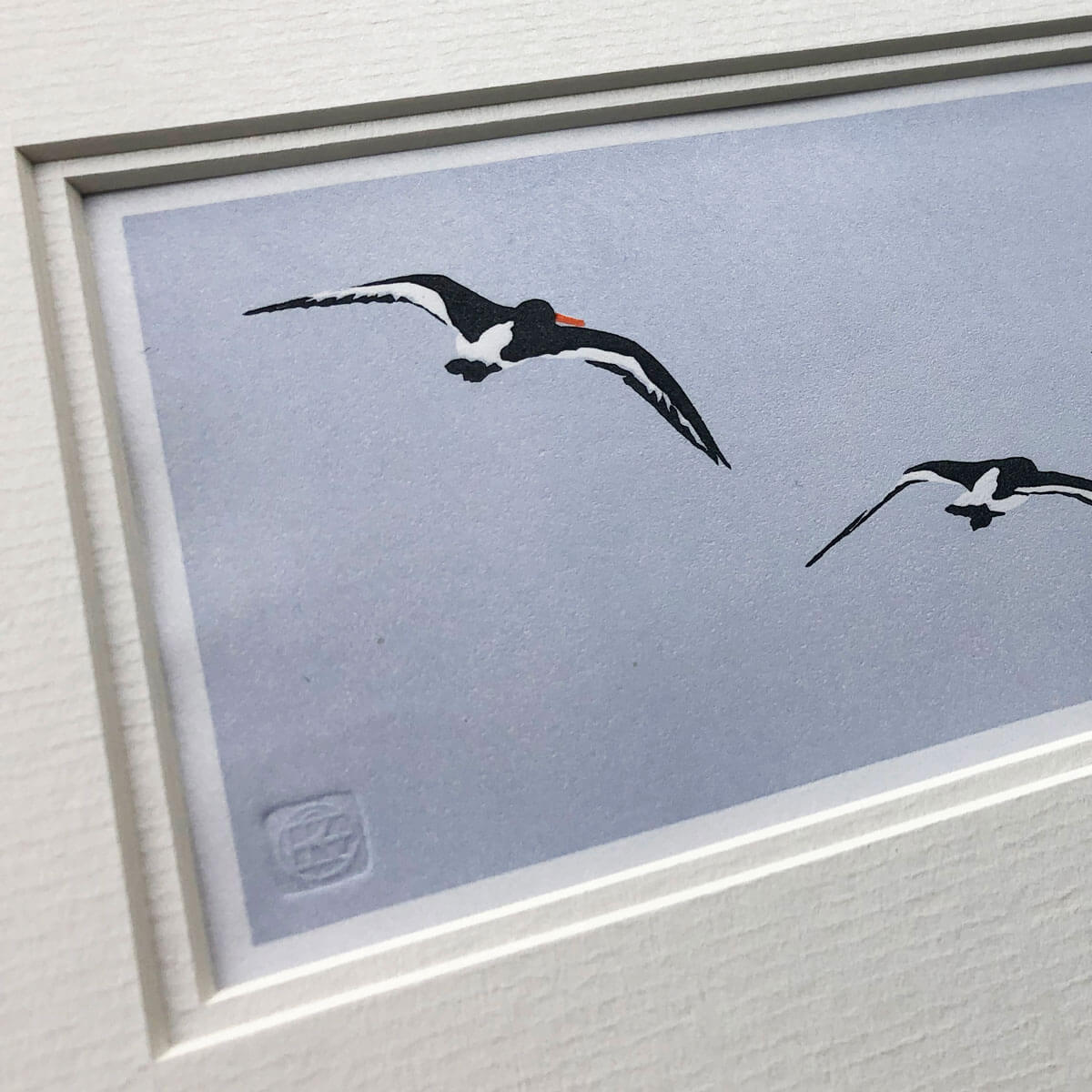 handmade linocut print of black and white oyster catcher birds in flight against pale blue sky background