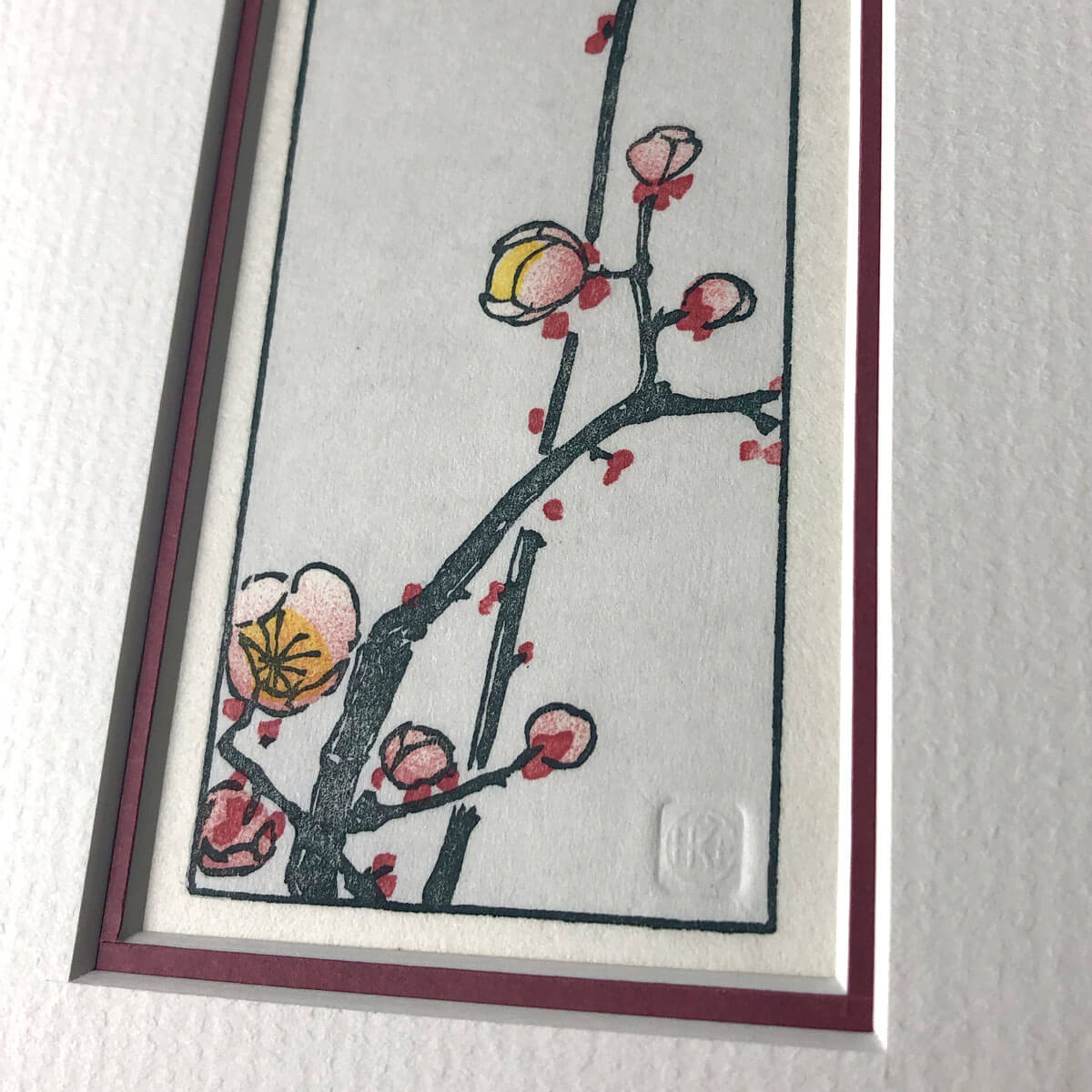 handmade woodblock print of slim branch with pale pink plum blossoms against a pale blue grey background