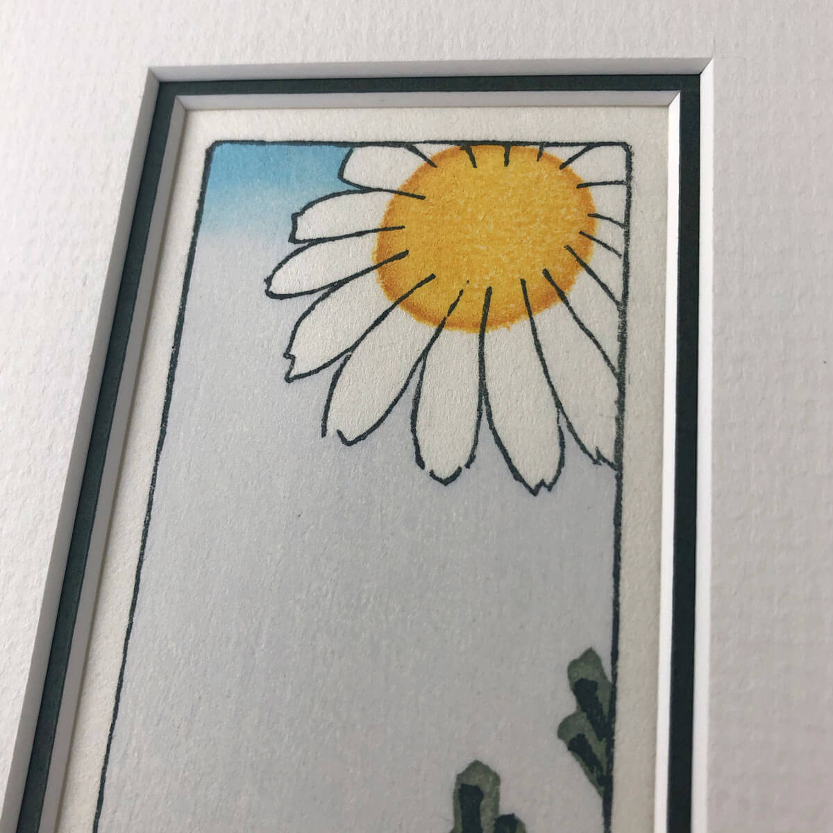 handmade woodblock print of a white daisy with yellow centre against pale blue grey background