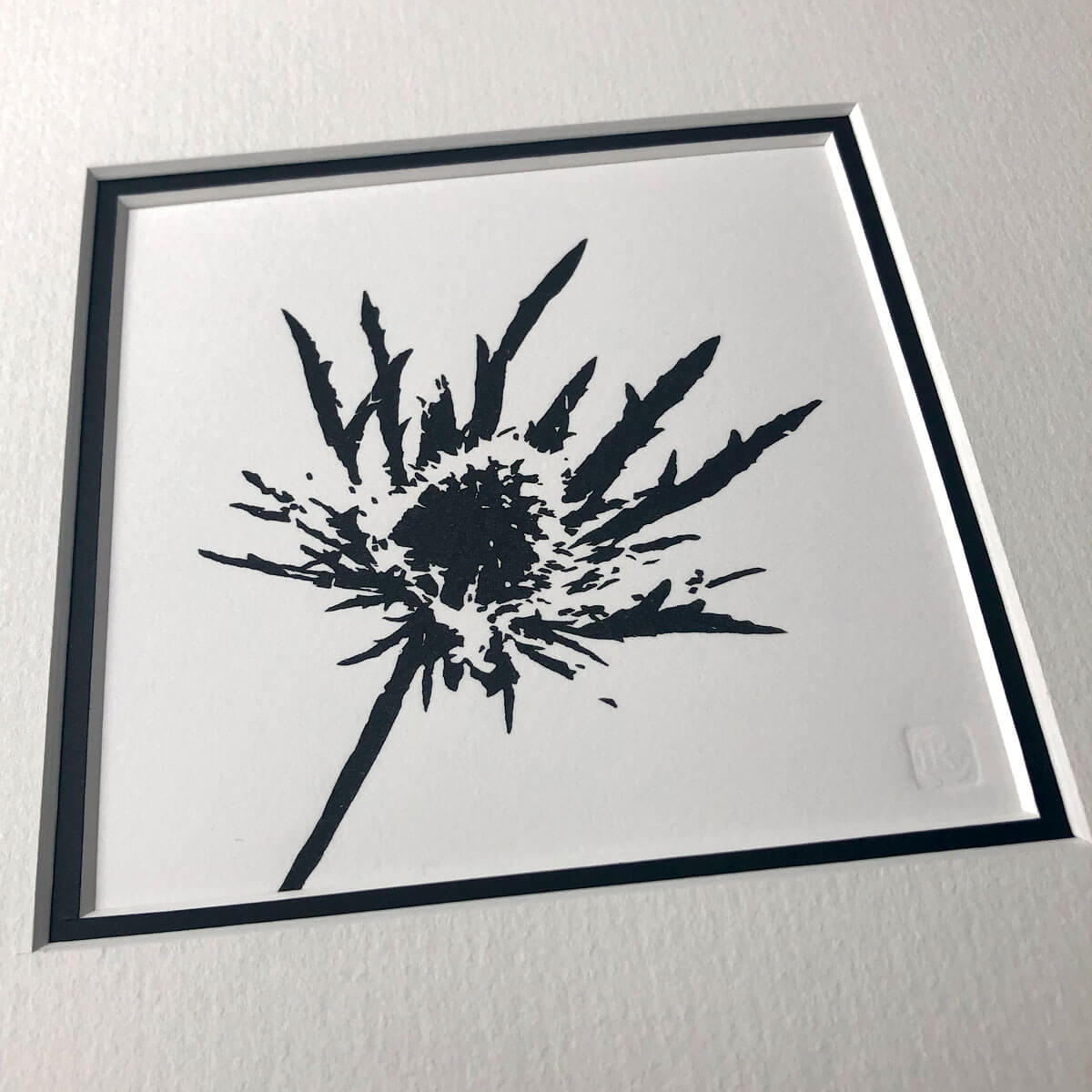 handmade woodblock print of a sea holly flowerhead in pure black against plain pale background